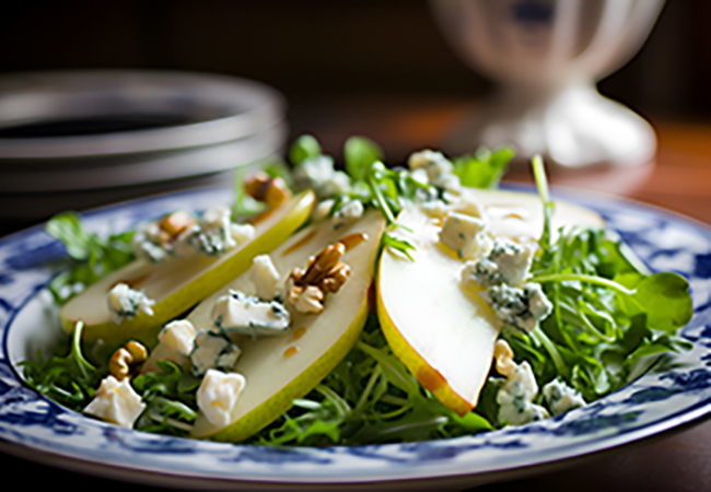 Pear and blue cheese salad on porcelain plate on rustic wooden table, close-up. Pear salad made from green salad leaves, rocket salad, slices of fresh pears, pieces of blue cheese, walnuts and honey